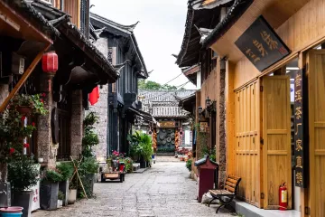 Scenic view of Shuhe Ancient Town in Lijiang, Yunnan, China - traditional Naxi architecture with stone bridges, flowing canals, and snow-capped Jade Dragon Mountain in background. UNESCO World Heritage Site showcasing well-preserved Tea Horse Road history.